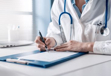 Arzt mit Stethoskop schreibt auf Klemmbrett im Büro – Symbolbild für medizinische Dokumentation und Verwaltung.