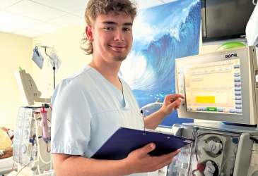 Pflegekraft bedient Dialysegerät und hält Klemmbrett – medizinische Tätigkeit in einer modernen Klinikumgebung.