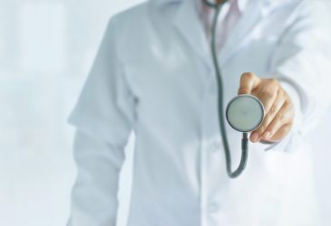 Arzt im weißen Kittel hält Stethoskop nach vorn, Symbolbild für medizinische Untersuchung und Patientenversorgung.