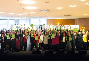 Feierliche Zeugnisübergabe: Absolventinnen und Absolventen halten Urkunden und Blumen bei Abschlussveranstaltung im Saal