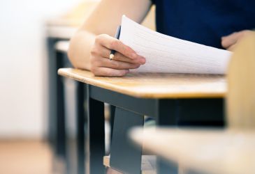 Schriftliche Prüfung im medizinischen Kontext: Hand mit Stift bearbeitet Prüfungsunterlagen an einem Schreibtisch.