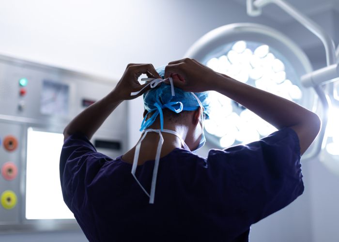 Chirurg bereitet sich im OP vor und bindet Haube, Operationssaal mit OP-Leuchte im Hintergrund